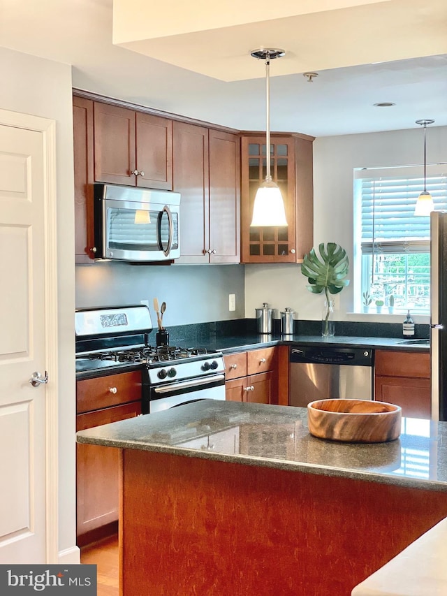 kitchen with hanging light fixtures, dark stone countertops, appliances with stainless steel finishes, and glass insert cabinets