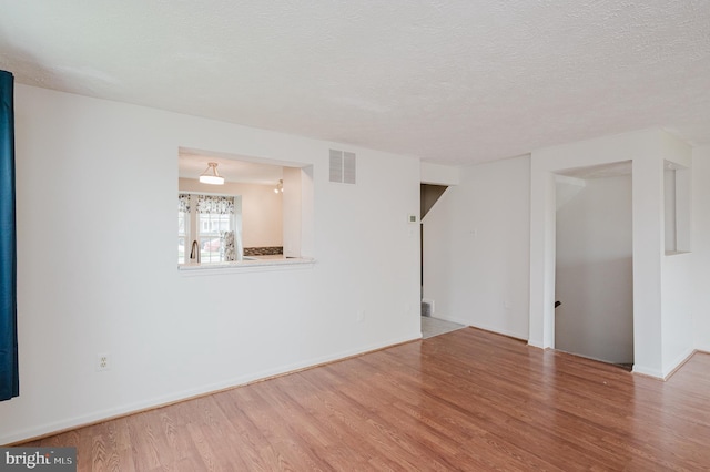 unfurnished living room featuring baseboards, wood finished floors, visible vents, and a textured ceiling