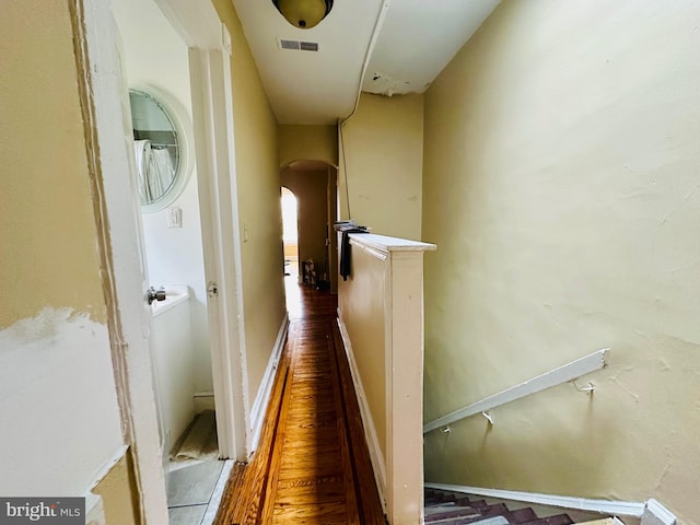 corridor with arched walkways, wood finished floors, and visible vents