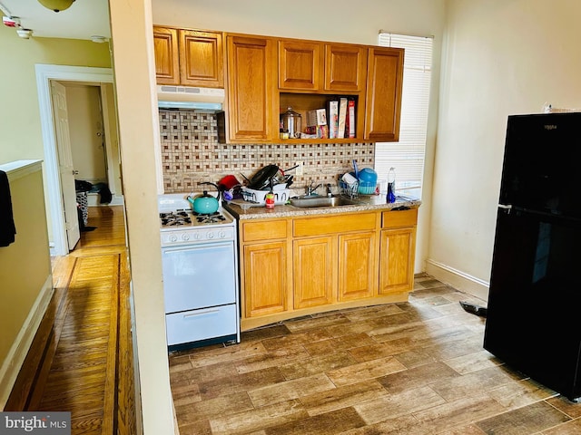 kitchen with freestanding refrigerator, backsplash, white gas range, under cabinet range hood, and a sink