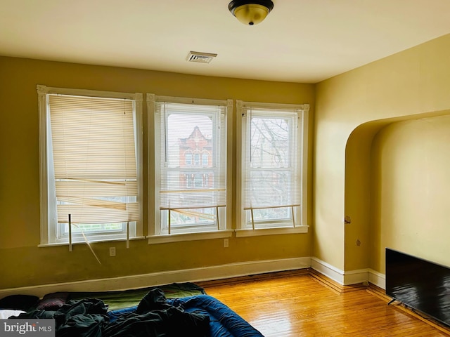 living area featuring visible vents, light wood-style flooring, arched walkways, and baseboards