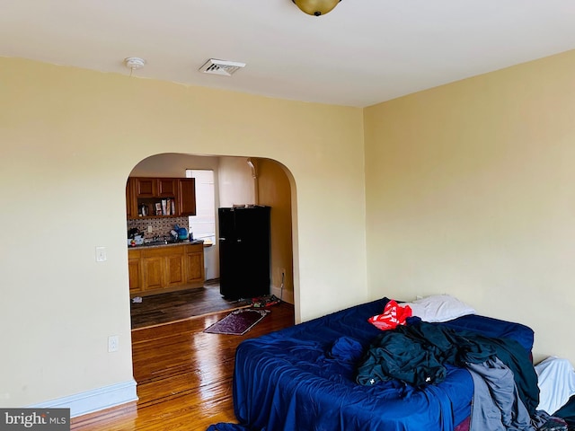 bedroom with freestanding refrigerator, dark wood-type flooring, arched walkways, visible vents, and baseboards