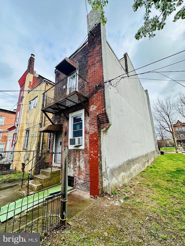 view of side of property featuring a balcony, stucco siding, a chimney, cooling unit, and brick siding
