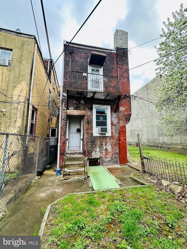 back of house featuring entry steps, fence, brick siding, and a balcony