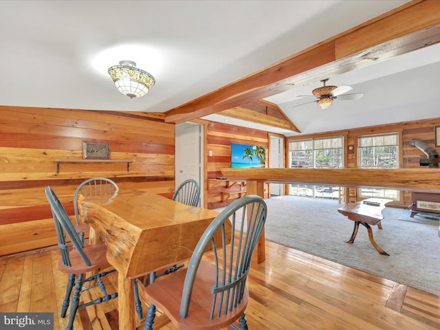 dining area with wooden walls, hardwood / wood-style floors, vaulted ceiling with beams, and a ceiling fan