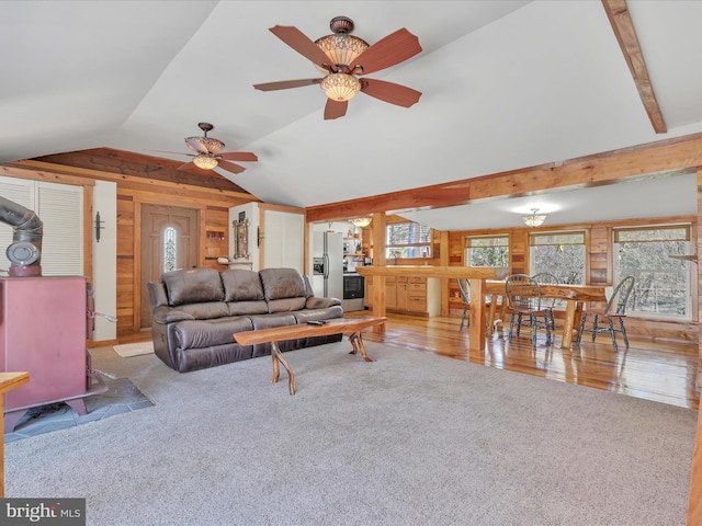 carpeted living area with vaulted ceiling, wood walls, and a ceiling fan
