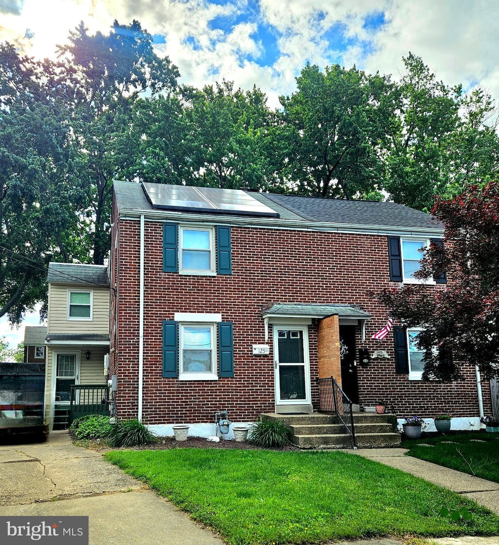 125 Denn Pl, Wilmington, DE 19804 - view of front facade featuring brick siding, a front lawn, and roof mounted solar panels