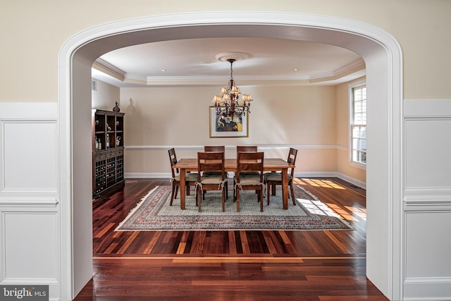 dining area featuring arched walkways, ornamental molding, a chandelier, wood finished floors, and baseboards