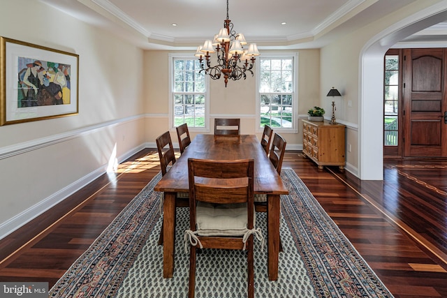 dining room with arched walkways, dark wood-style floors, a tray ceiling, and an inviting chandelier