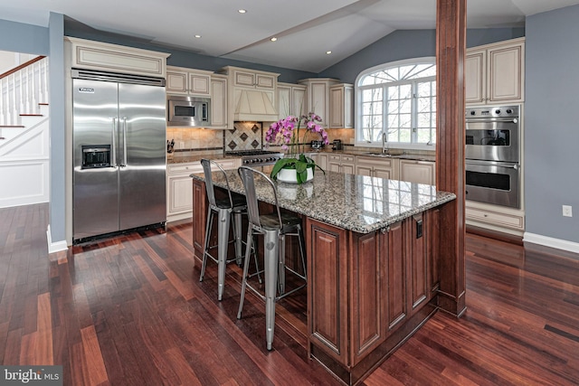 kitchen with dark wood-type flooring, built in appliances, a sink, and cream cabinets