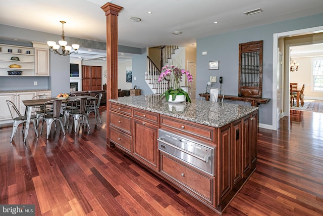 kitchen featuring a notable chandelier, light stone counters, a warming drawer, dark wood-type flooring, and ornate columns