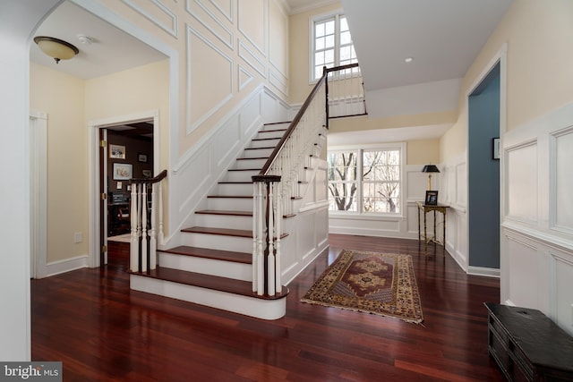 stairs featuring arched walkways, wood finished floors, baseboards, and a towering ceiling