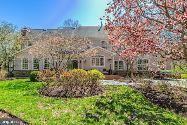 rear view of house with a yard, a patio, stone siding, and a chimney