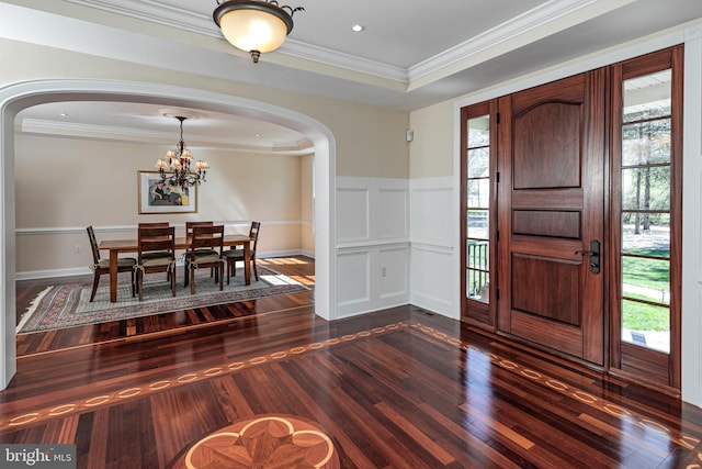 foyer entrance featuring a chandelier, arched walkways, dark wood-style floors, and ornamental molding
