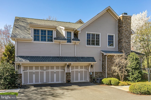 view of front of house with a chimney, stone siding, a garage, and aphalt driveway