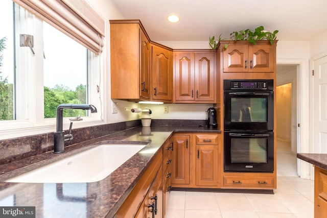 kitchen featuring a sink, dark stone countertops, light tile patterned flooring, brown cabinets, and recessed lighting