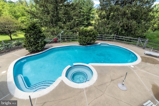 view of swimming pool with a fenced backyard, a pool with connected hot tub, view of scattered trees, and a patio area