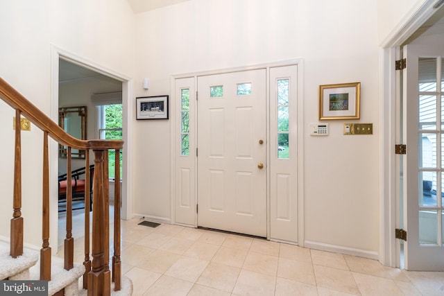 foyer entrance featuring baseboards, light tile patterned floors, stairway, and a high ceiling