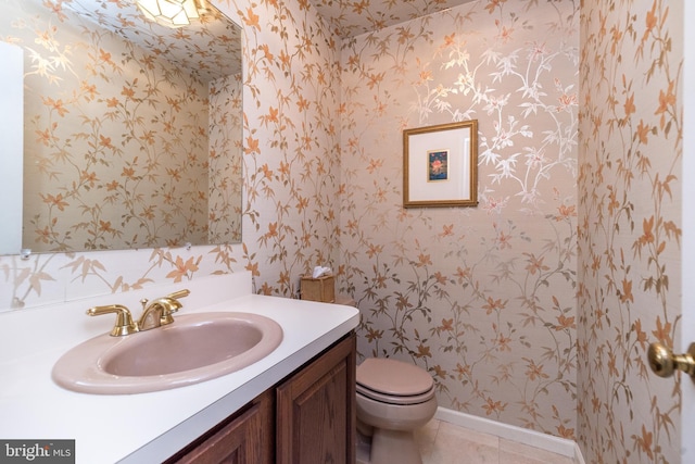 half bathroom with wallpapered walls, vanity, toilet, baseboards, and tile patterned floors