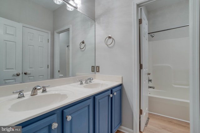 full bath with double vanity, a sink, shower / bath combination, and wood finished floors
