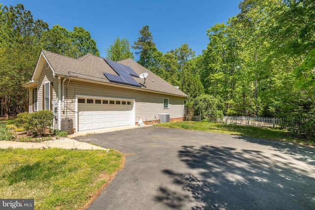 view of side of home featuring aphalt driveway, fence, cooling unit, an attached garage, and solar panels