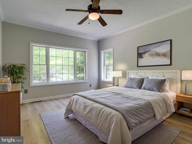 bedroom featuring a ceiling fan, visible vents, crown molding, baseboards, and light wood-style flooring