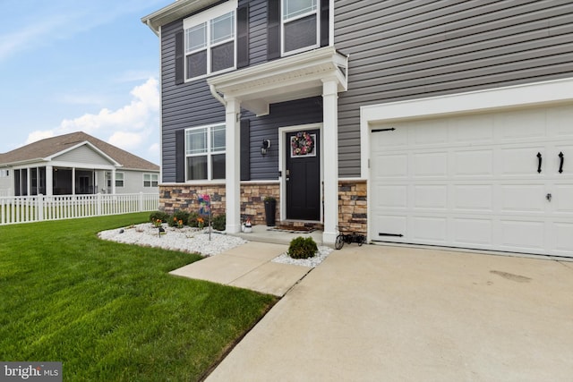 entrance to property with a yard, driveway, stone siding, and fence