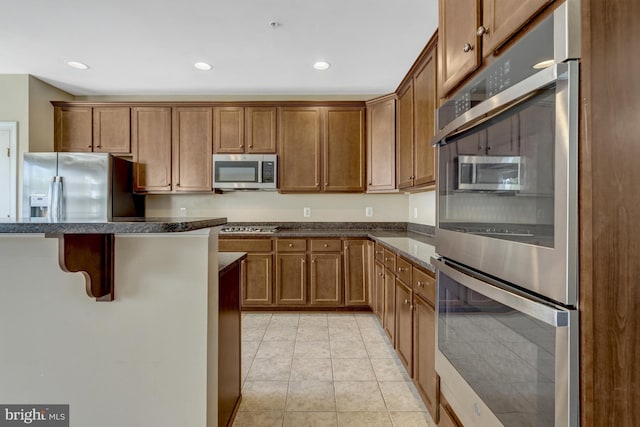 kitchen featuring light tile patterned flooring, brown cabinetry, stainless steel appliances, recessed lighting, and a kitchen bar