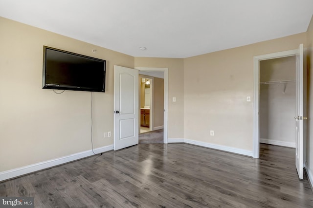 unfurnished bedroom featuring baseboards, a closet, wood finished floors, and a spacious closet