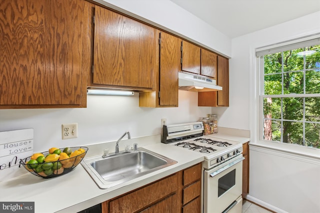 kitchen with under cabinet range hood, gas range gas stove, a sink, light countertops, and brown cabinets