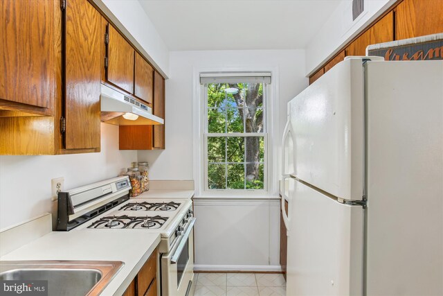 kitchen featuring white appliances, under cabinet range hood, brown cabinets, light countertops, and baseboards