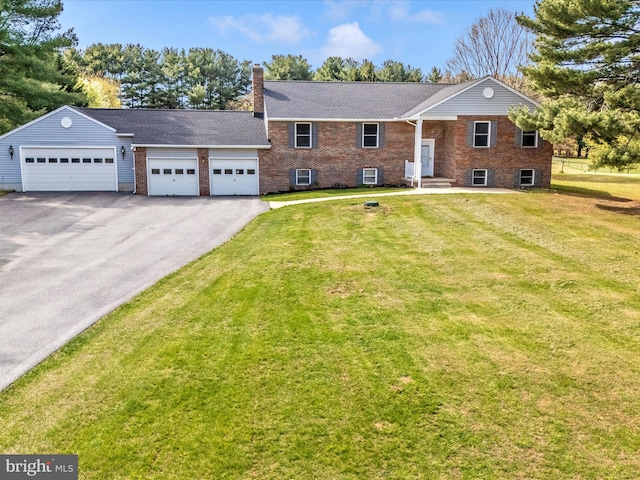 view of front of house featuring a front yard, brick siding, an attached garage, a chimney, and driveway