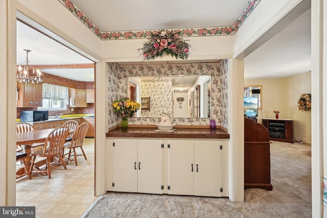 bar with light colored carpet, black microwave, tasteful backsplash, and an inviting chandelier