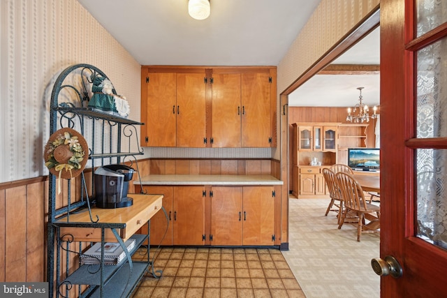 kitchen with a chandelier, wallpapered walls, brown cabinets, light floors, and light countertops