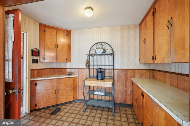 kitchen featuring light floors, wallpapered walls, a wainscoted wall, and light countertops