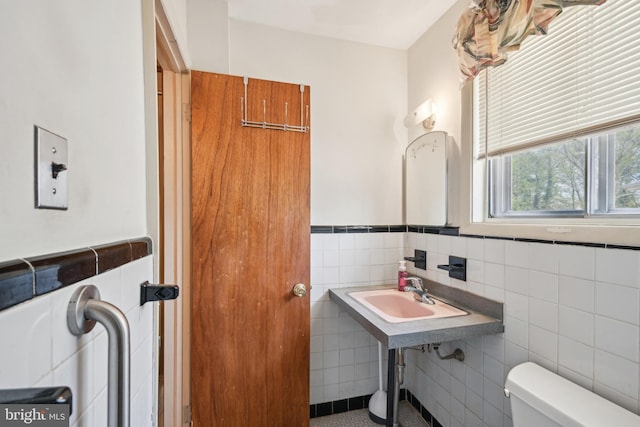half bathroom featuring a sink, toilet, tile walls, wainscoting, and tile patterned flooring