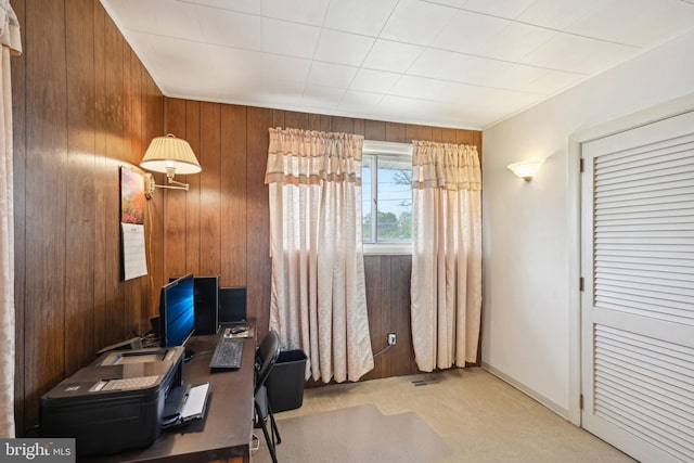 carpeted home office with visible vents, wooden walls, and baseboards