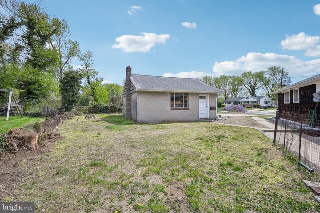 view of home's exterior featuring a chimney, fence, concrete block siding, and a yard