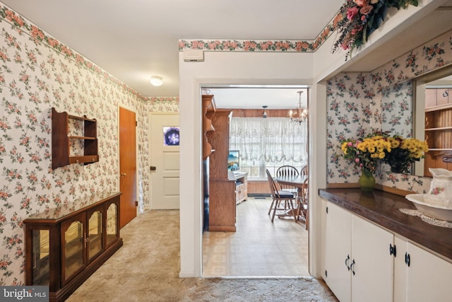 hall featuring wallpapered walls, light carpet, and an inviting chandelier