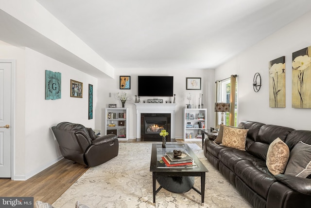 living area with baseboards, a fireplace with flush hearth, and wood finished floors