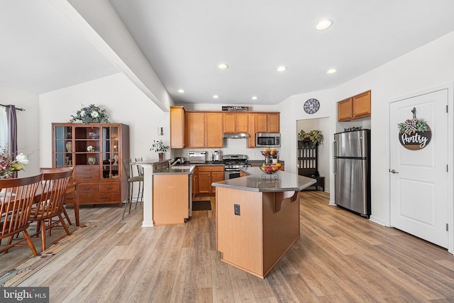 kitchen featuring a kitchen breakfast bar, dark countertops, appliances with stainless steel finishes, light wood-style floors, and recessed lighting
