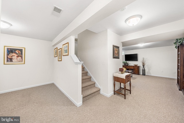 finished below grade area featuring baseboards, visible vents, light carpet, and stairway