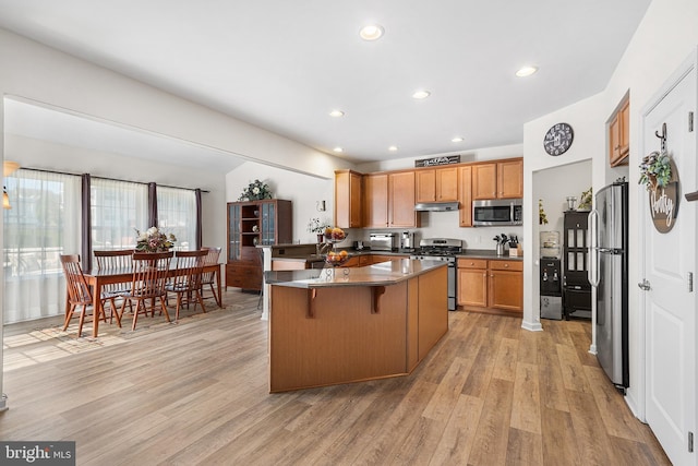 kitchen featuring a breakfast bar area, brown cabinets, light wood finished floors, under cabinet range hood, and stainless steel appliances