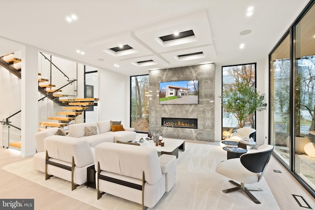 living room featuring coffered ceiling, a fireplace, plenty of natural light, and stairway