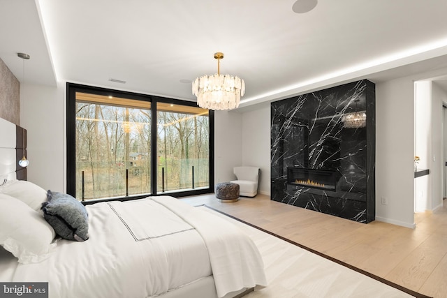 bedroom with a premium fireplace, wood finished floors, a notable chandelier, and floor to ceiling windows