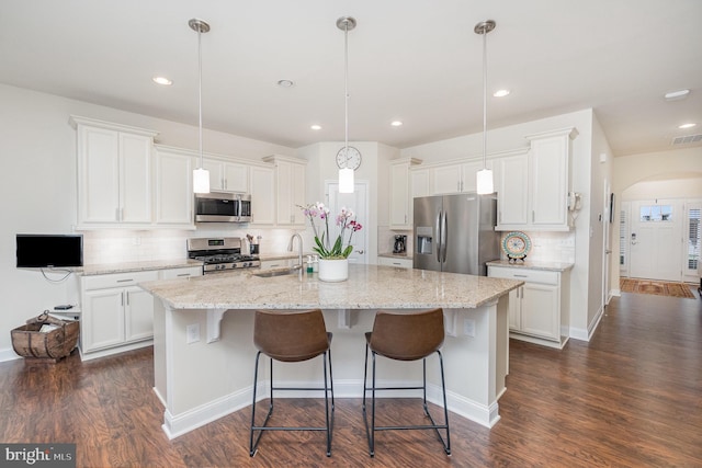 kitchen with tasteful backsplash, arched walkways, a sink, an island with sink, and stainless steel appliances