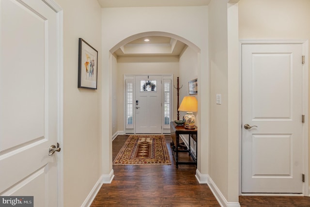 foyer featuring a tray ceiling, arched walkways, baseboards, and dark wood-style floors