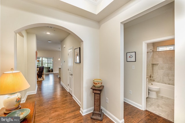 hall with arched walkways, baseboards, and wood finished floors