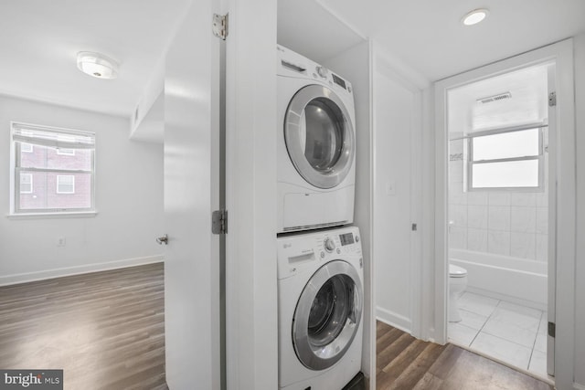 laundry area featuring baseboards, dark wood-type flooring, stacked washing maching and dryer, and laundry area
