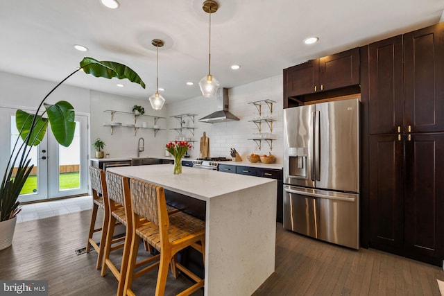 kitchen with stainless steel appliances, open shelves, wall chimney range hood, a sink, and dark wood-type flooring